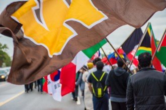 Decorative: W flag waves in front of flags from around the world carried by international students at WMU.