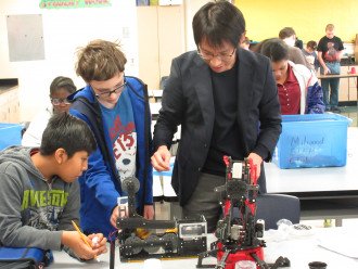 Dr. Matsumura works on a robot with two male high school students.