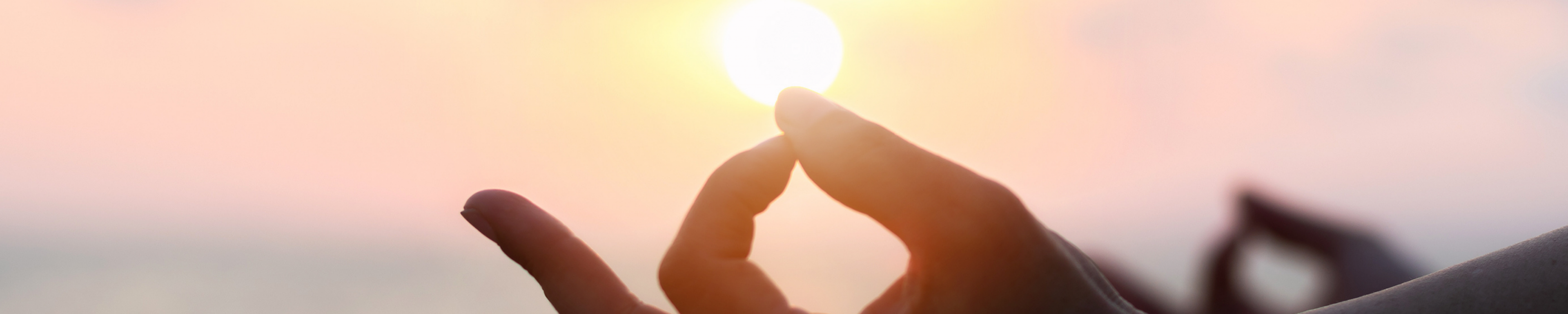 hand in a yoga mudra position resting on a knee in a silhouette against a sunset