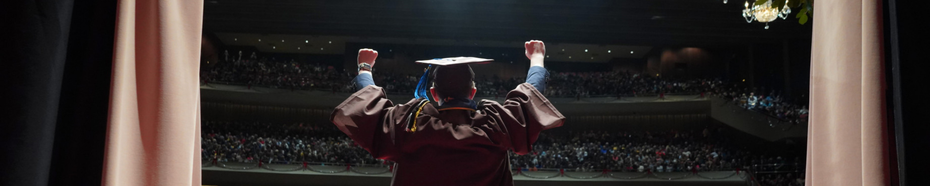 A graduate holds his arms up as he walks onto the stage.