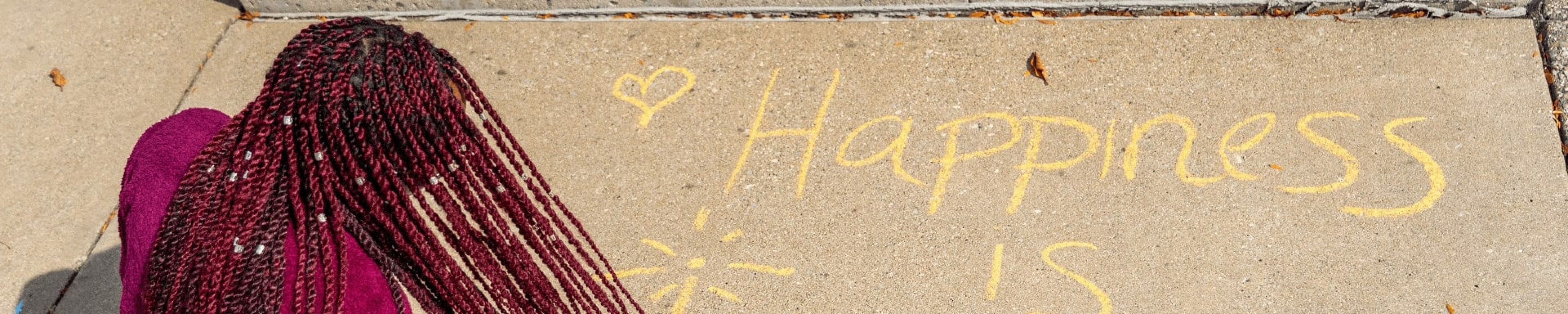 a student writes a "happiness" message in chalk on campus