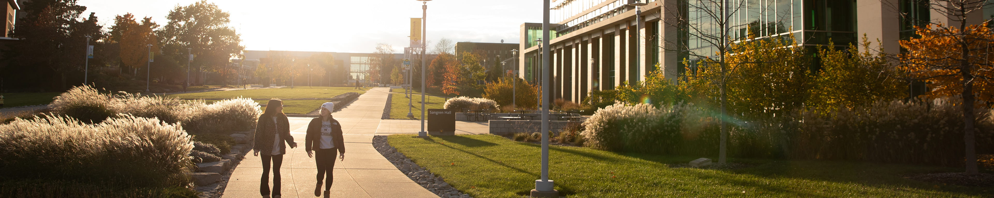 Two students walking next to Sangren Hall at sunset.