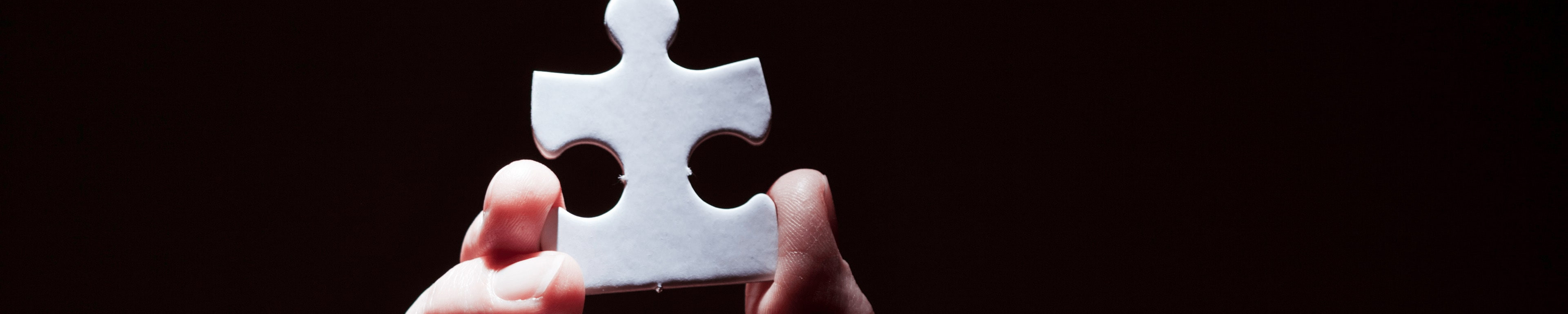 A single puzzle piece being held up by some fingers. 