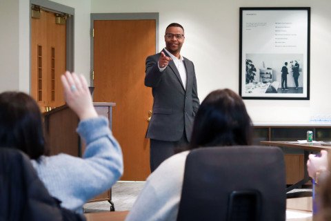 Professor in suit calling on student who has hand raised.