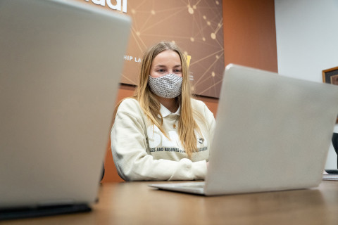 Student wearing mask sitting at laptop in sales lab