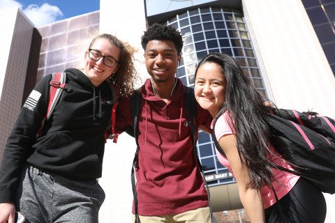 Three students near the library excited to confirm enrollment.