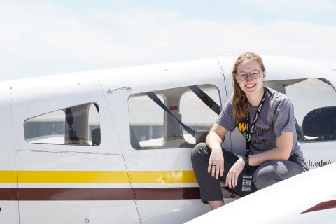 Female student looking at the camera, sitting on a small aircraft wing.