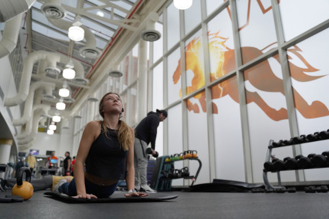 A young woman stretches on a mat in a gym.