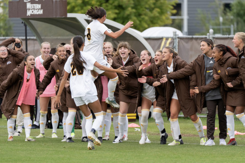 A soccer player jumps into the air as her teammates stand in a line cheering.