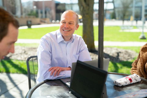 Dr. Brian Gogan sitting with a laptop outside.