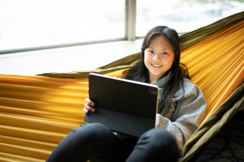 A student holding a laptop in a hammock.