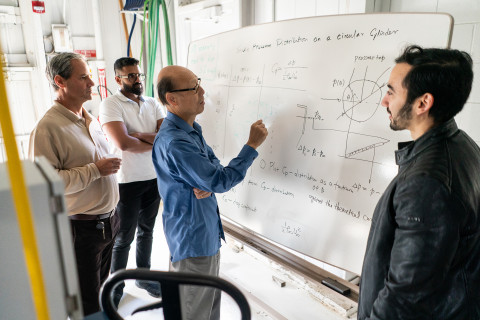 A graduate student in engineering discussing at the whiteboard with professors.