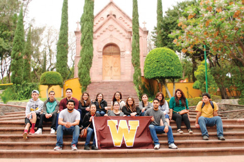 Students sitting on stairs outside of a building holding a Western flag