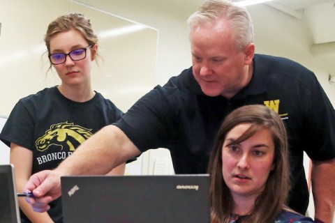 Dr. Steven Butt points to a laptop screen as two students look on