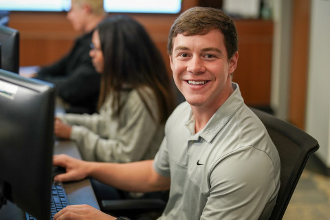 Student smiling at camera while working in computer lab
