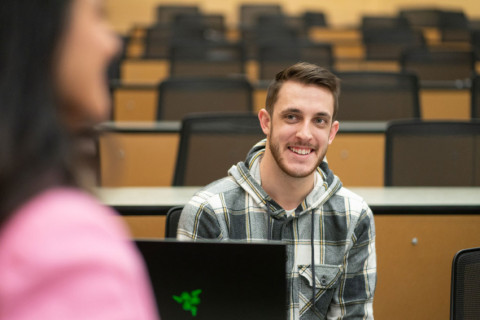 Students sitting in class smiling with professor in foreground