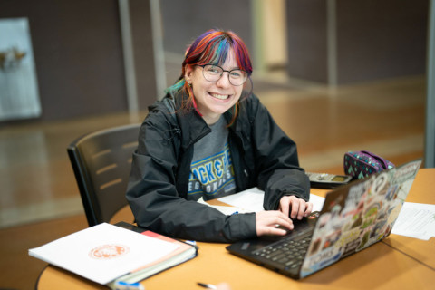 Student in study lounge with laptop smiling at camera