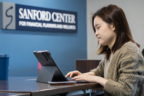 Student working at laptop with Sanford Center sign in background