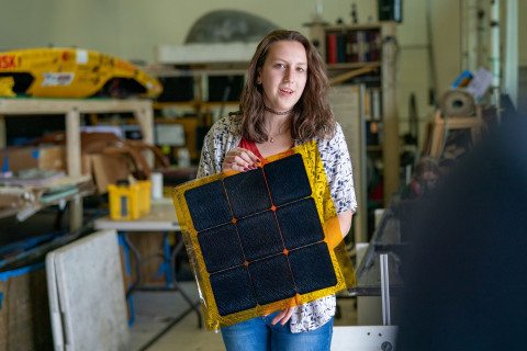 Engineering student displaying solar panel in lab.