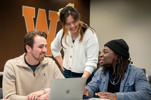 Three students gathered around a laptop
