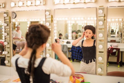 woman in period costume looking in dressing room mirror.