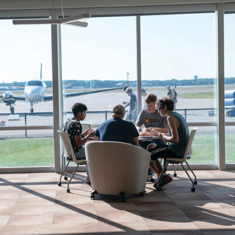 Students sit around a table looking out windows at an airplane.