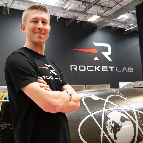 Greg Neff crosses his arms over his chest while standing in front of a wall that says Rocket Lab.