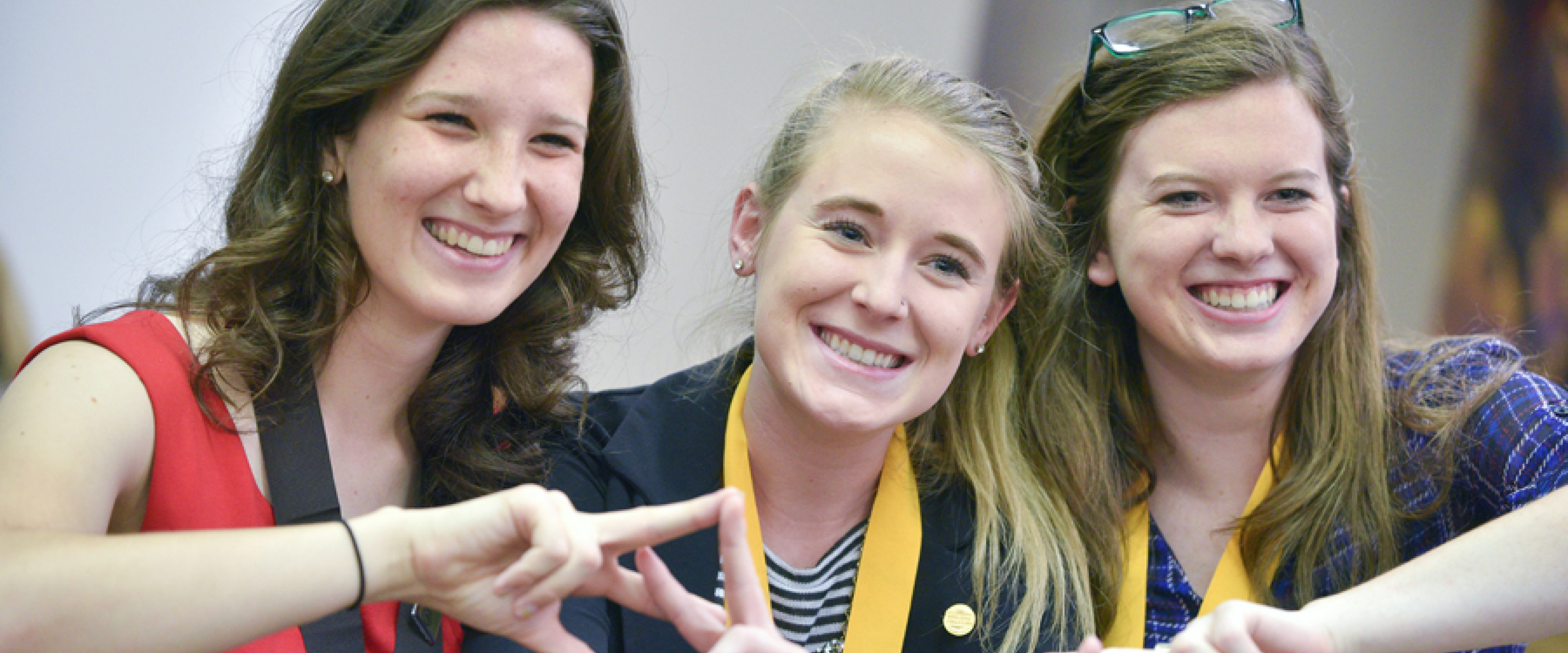 Three female honors students smiling and holding their hands up. 