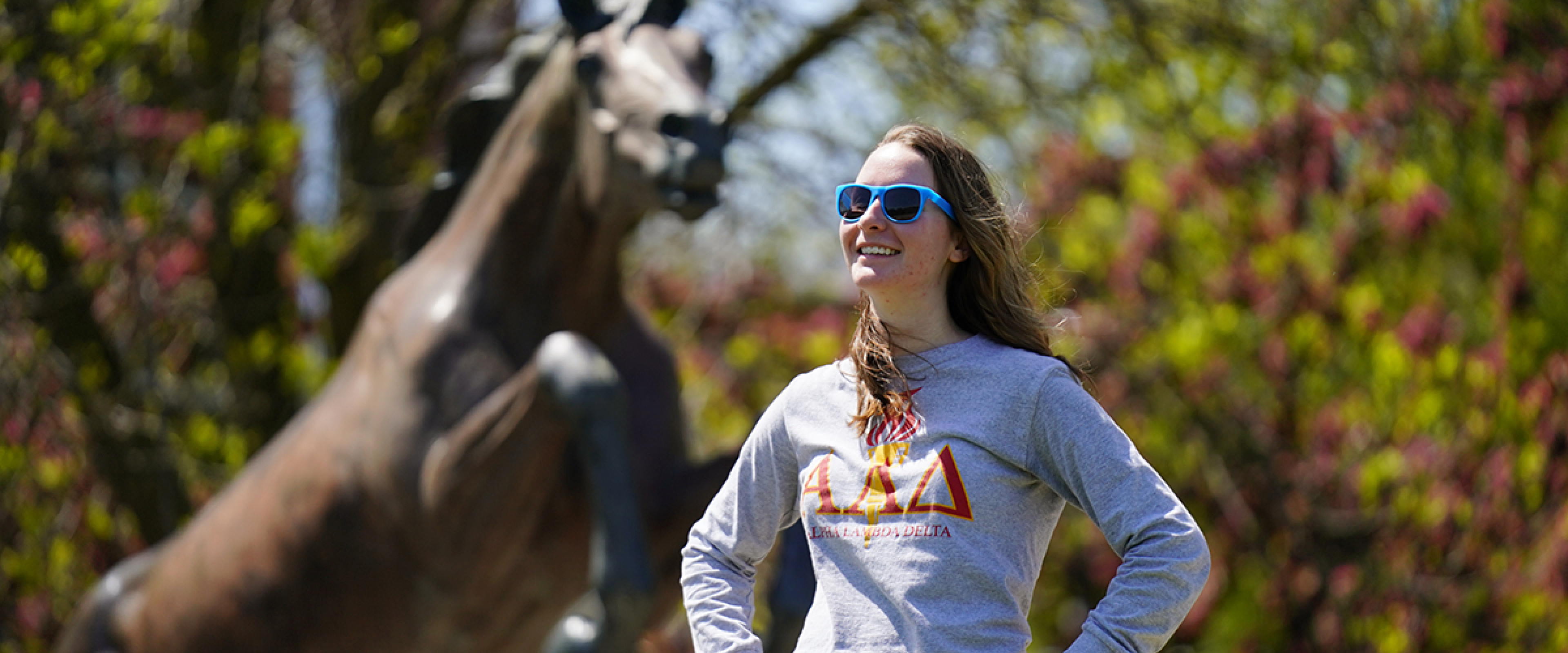 A student wearing an ALD shirt standing in front of the Bronco statue.