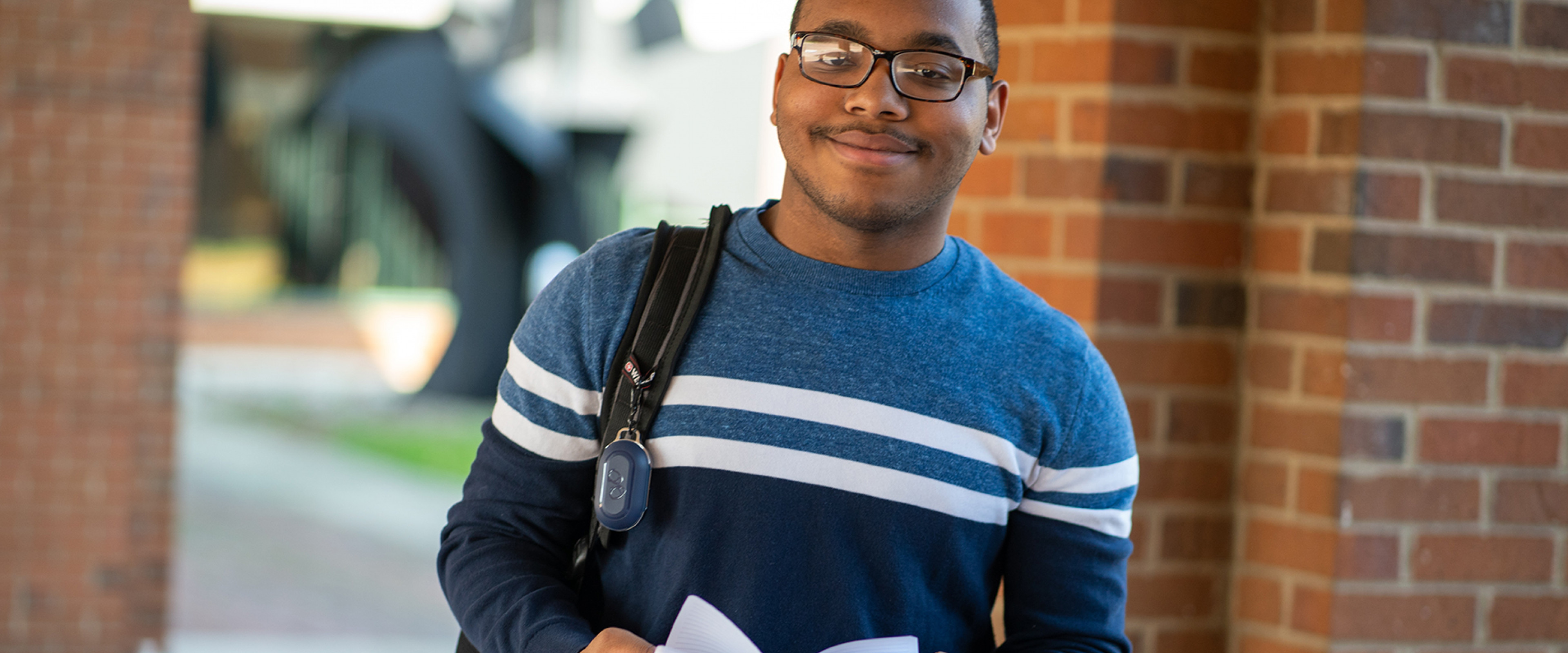 Pictured is a student standing outside of the business college holding a book and smiling