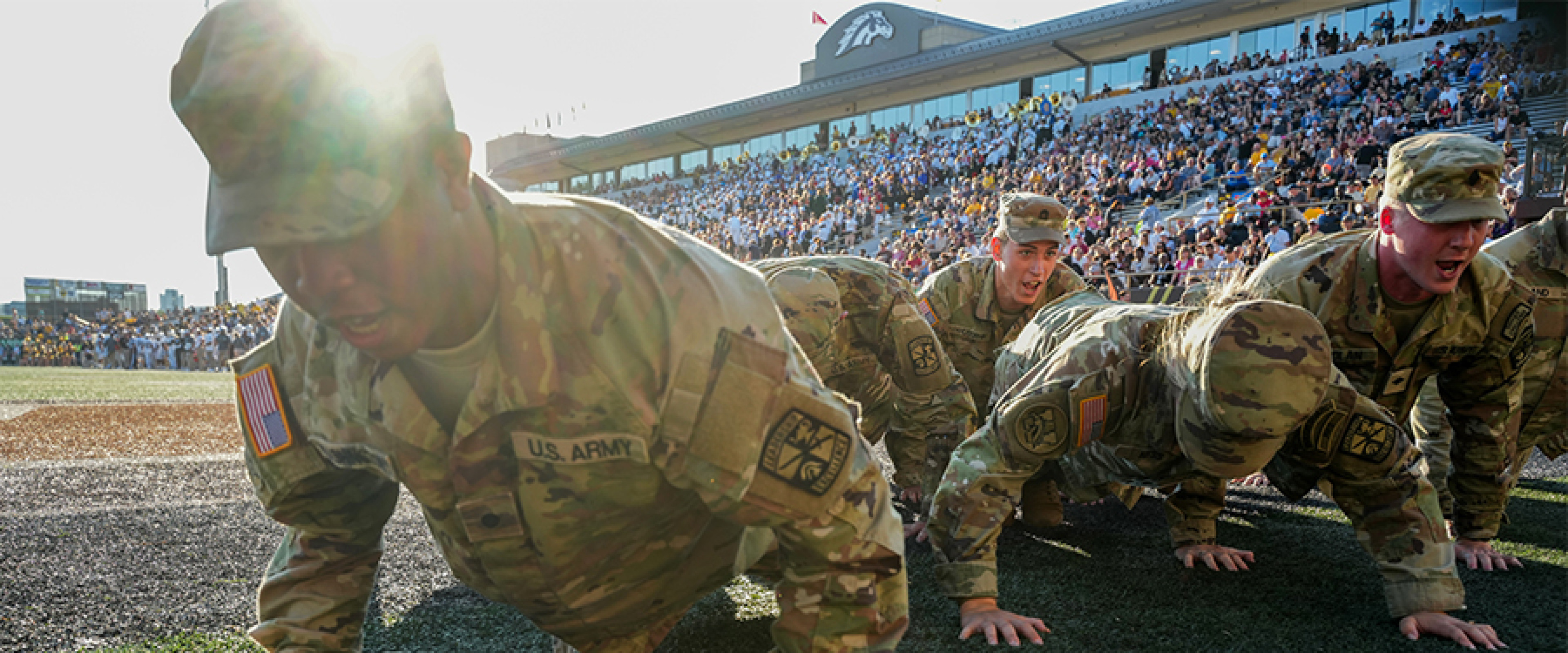 Cadets in uniform doing pushups in the end zone of a WMU football game.