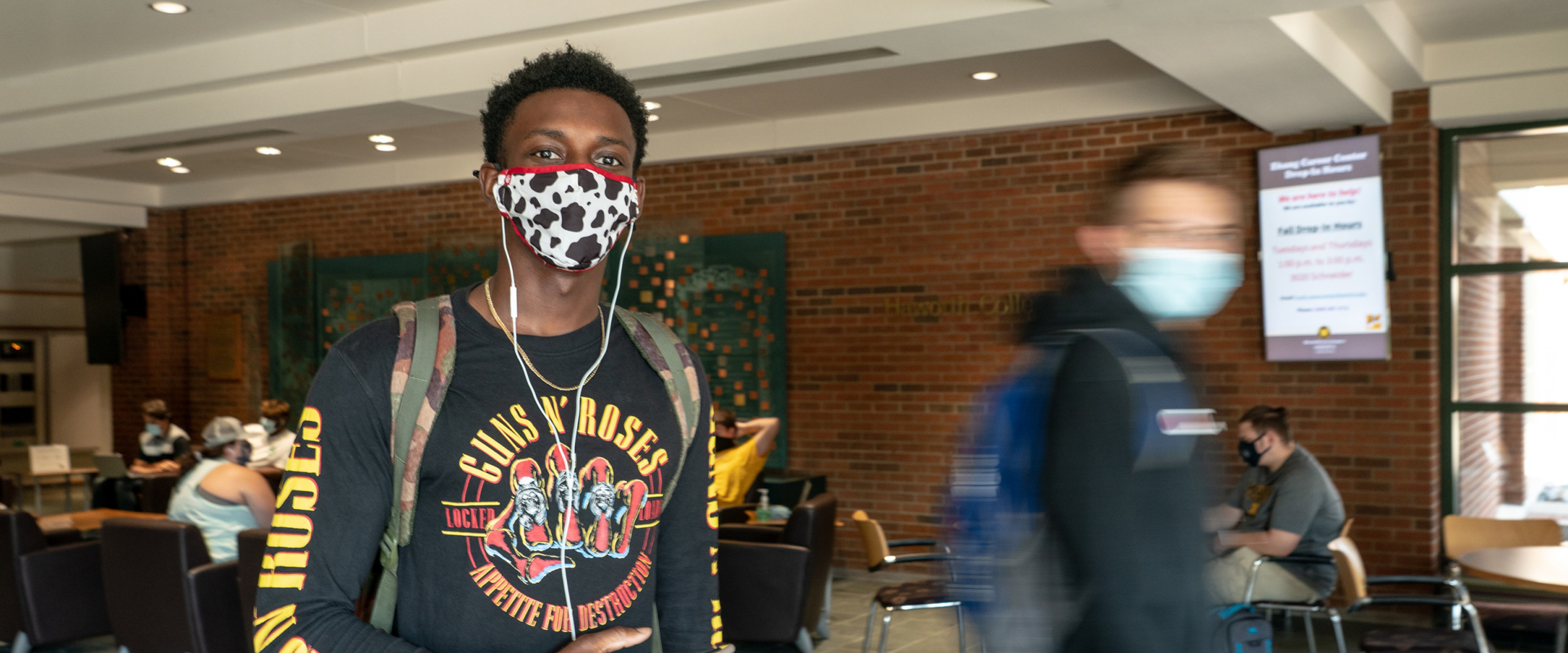 A student, wearing a mask and earphones, walks through the lobby of the Haworth College of Business.