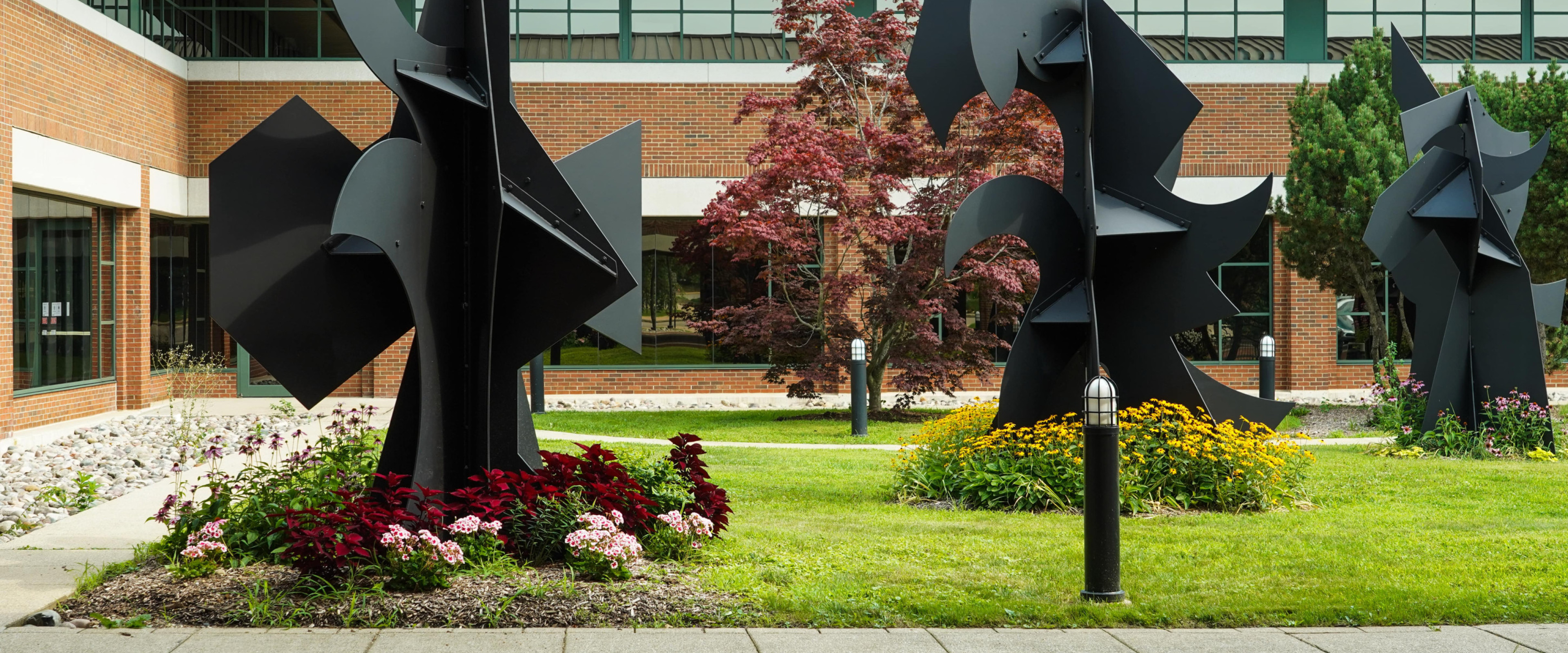 The Haworth College of Business courtyard has three large bronze abstract sculptures surrounded by flowers.