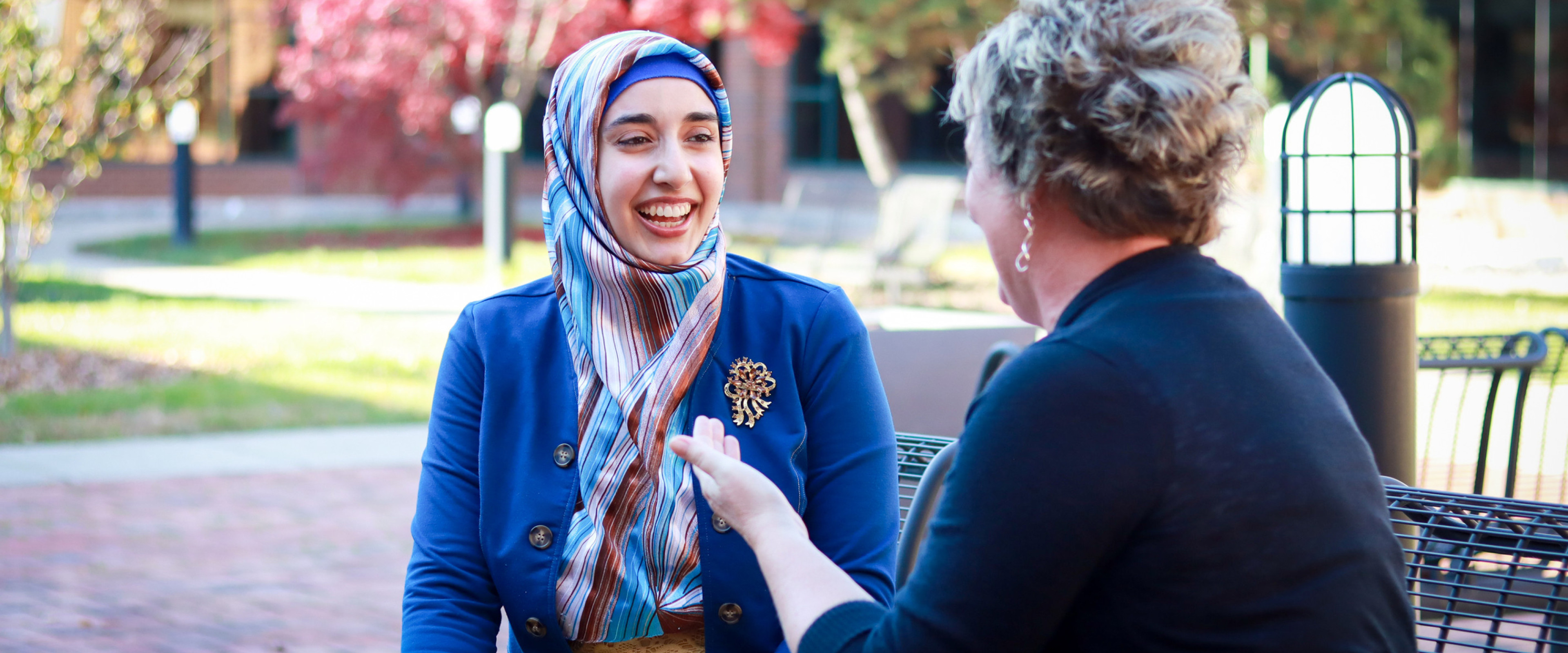 A student, wearing a headscarf, and Dr. Joann Atkin are chatting in the Haworth College of Business courtyard.