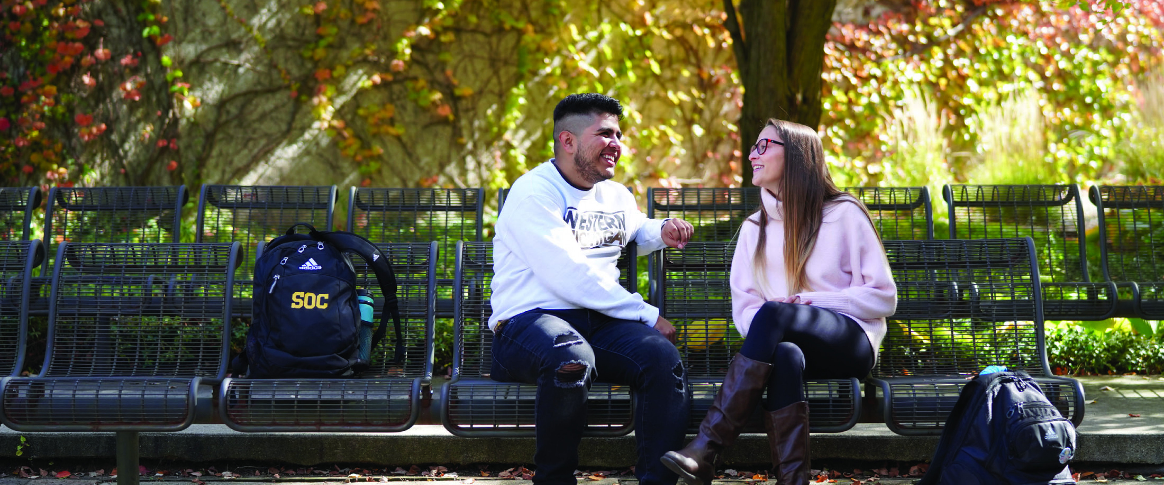 Students on campus on a bench, fall day.