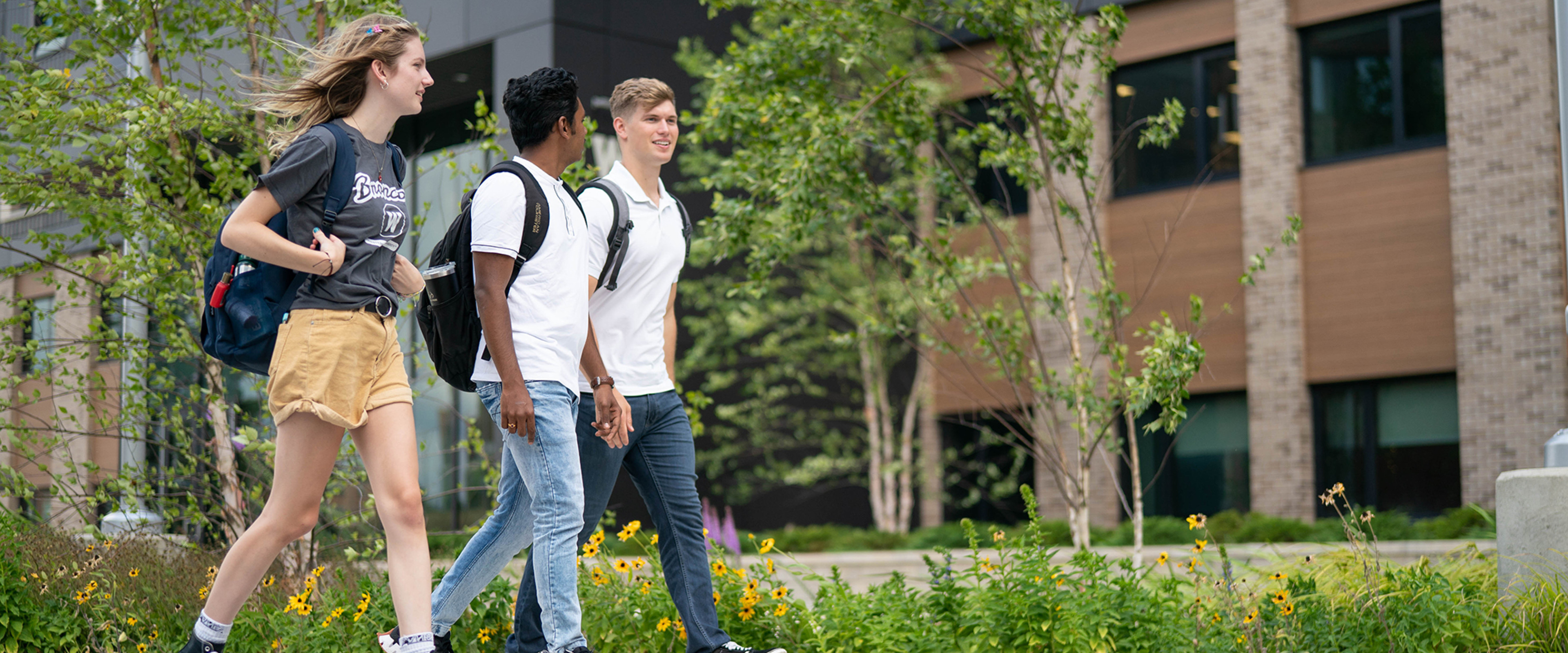 Three students, a female, two males walking on campus in front of Arcadia Flats.