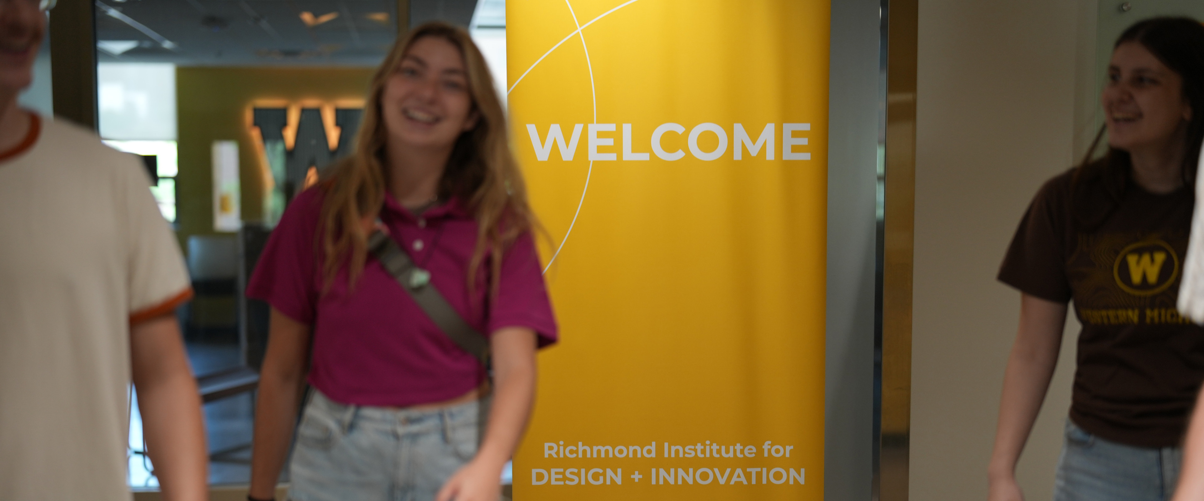 Students walking in front of a Welcome sign in the Richmond Institute for Design + Innovation.