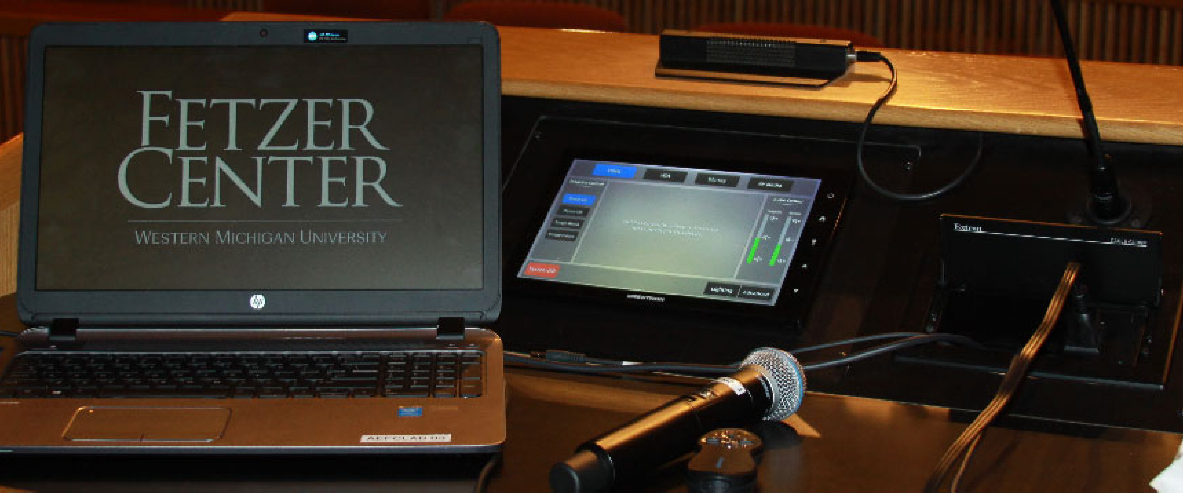 A laptop with Fetzer Center screen savor on a podium with microphone