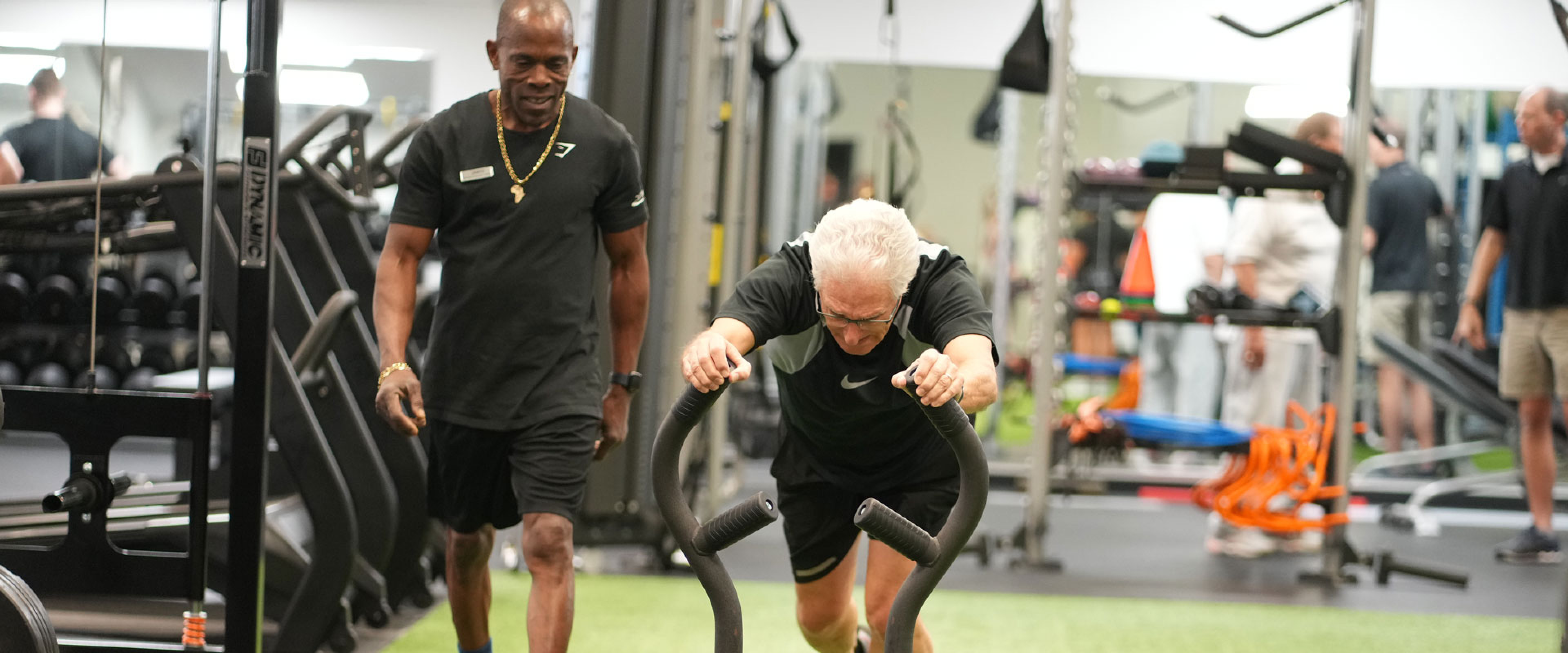 Black personal trainer assisting an older gentleman on the turf