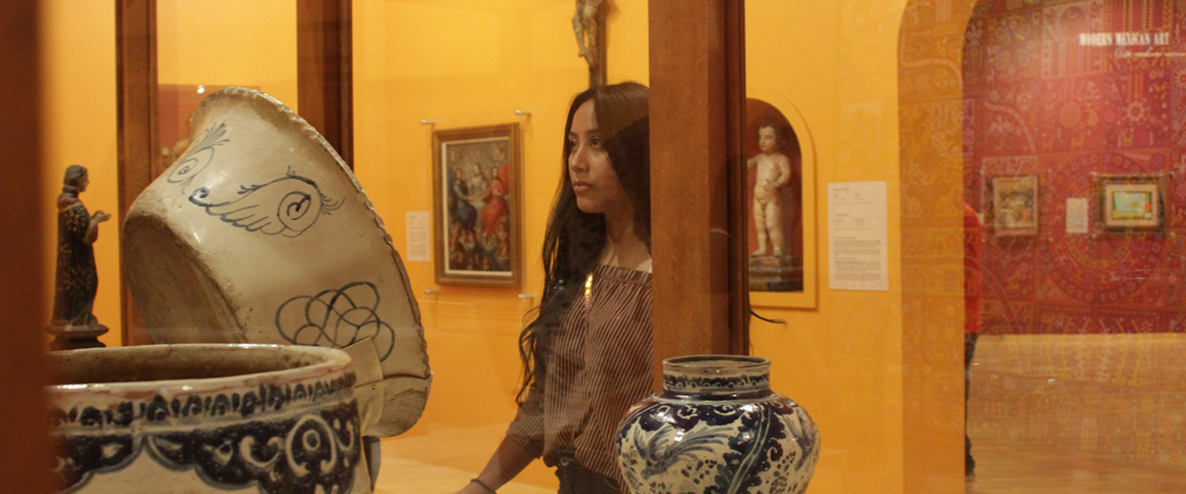 Student standing and looking into glass case with Mexican artifacts.