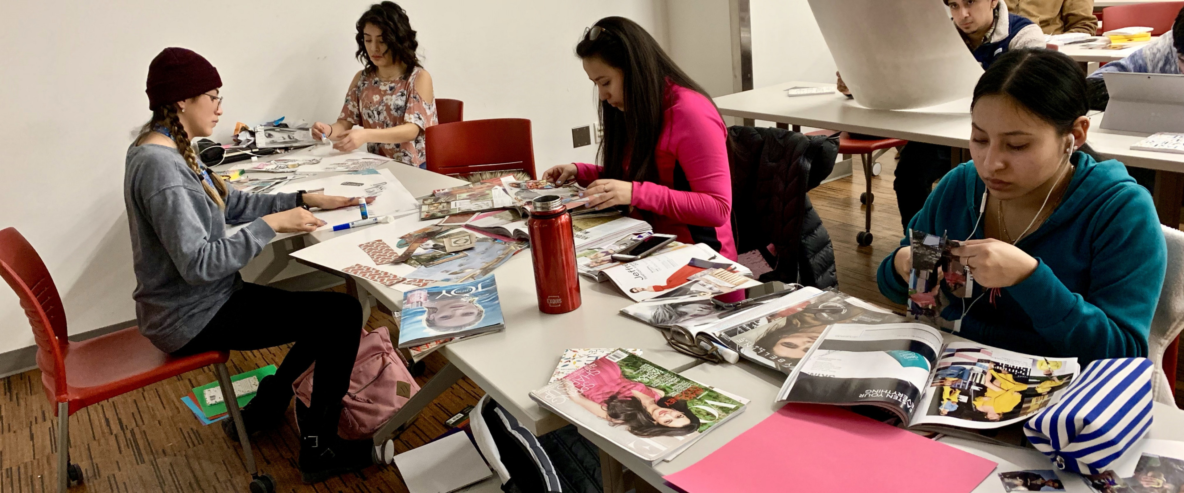 Students sitting at a long table cutting out images from magazines.