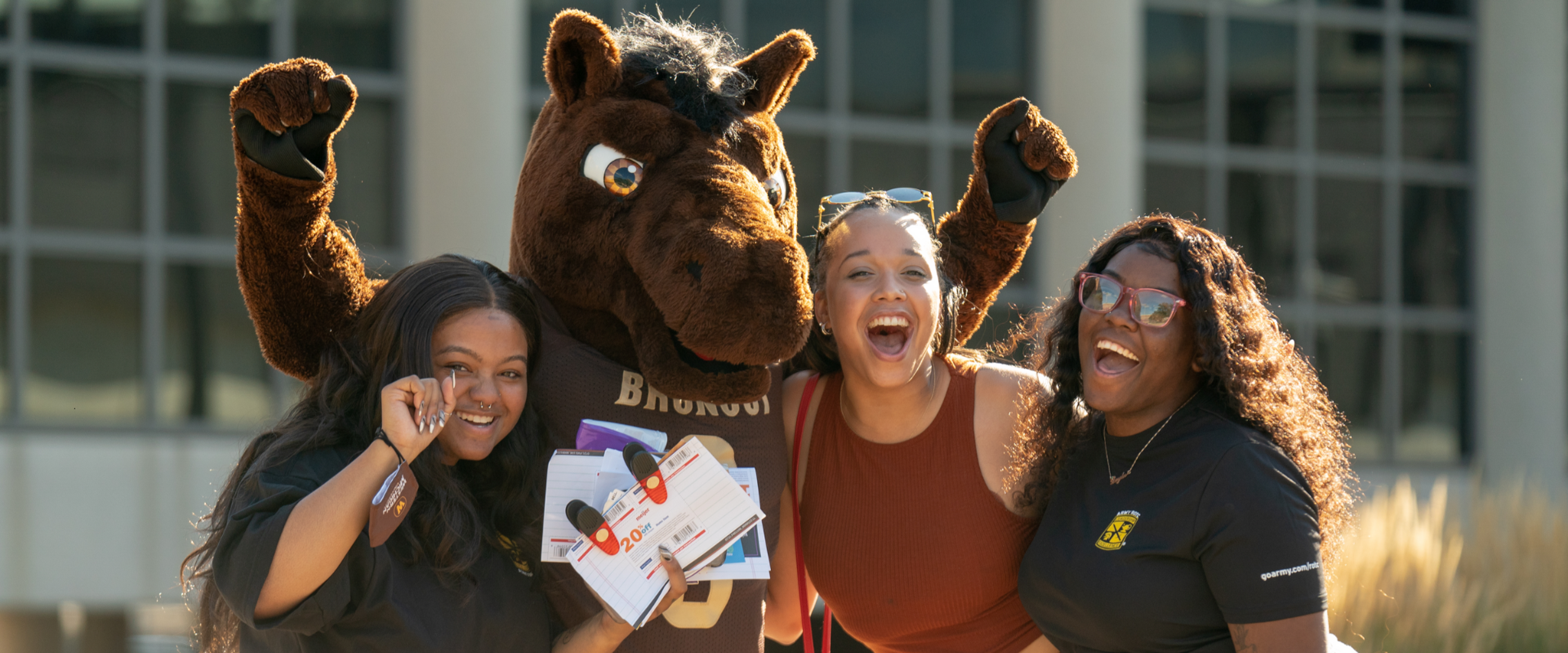 Three smiling students posing with Buster Bronco.