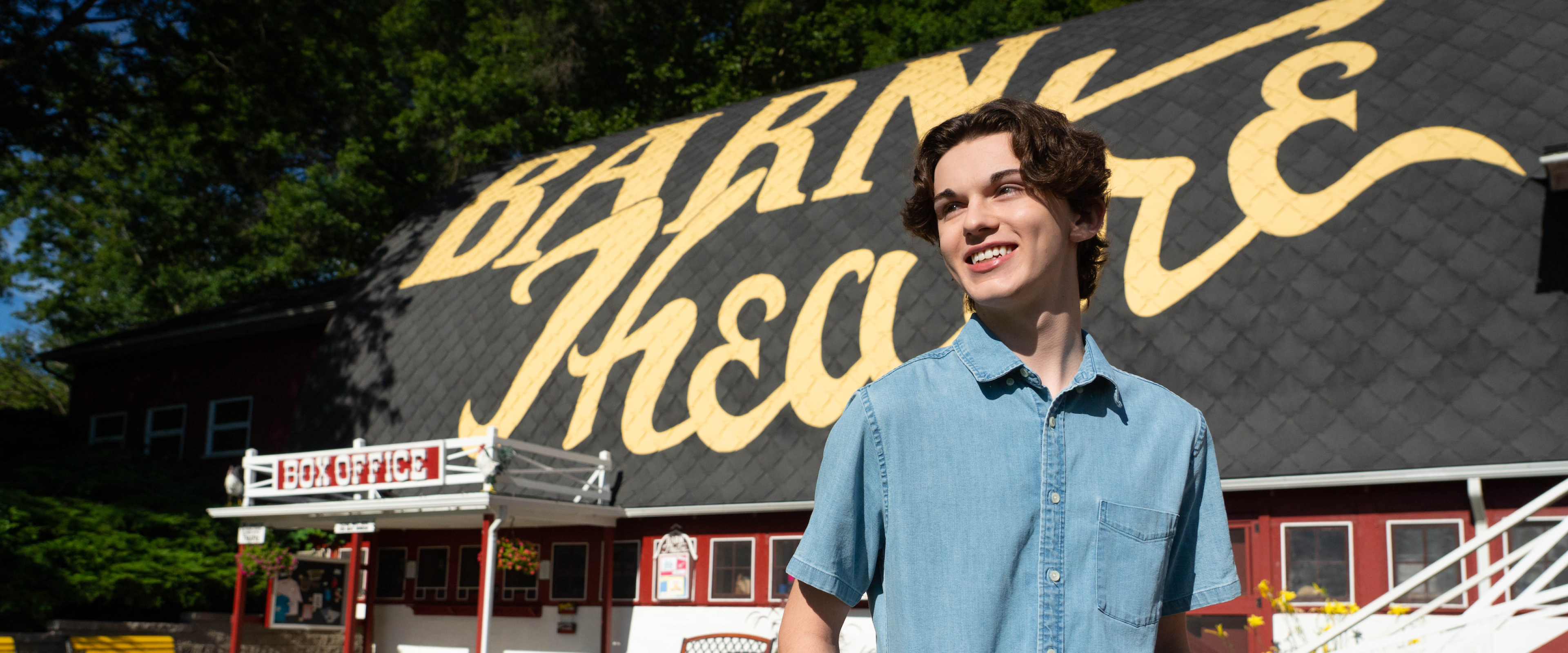 Jack Austin smiles and looks off into the distance while standing in front of the Barn Theatre.