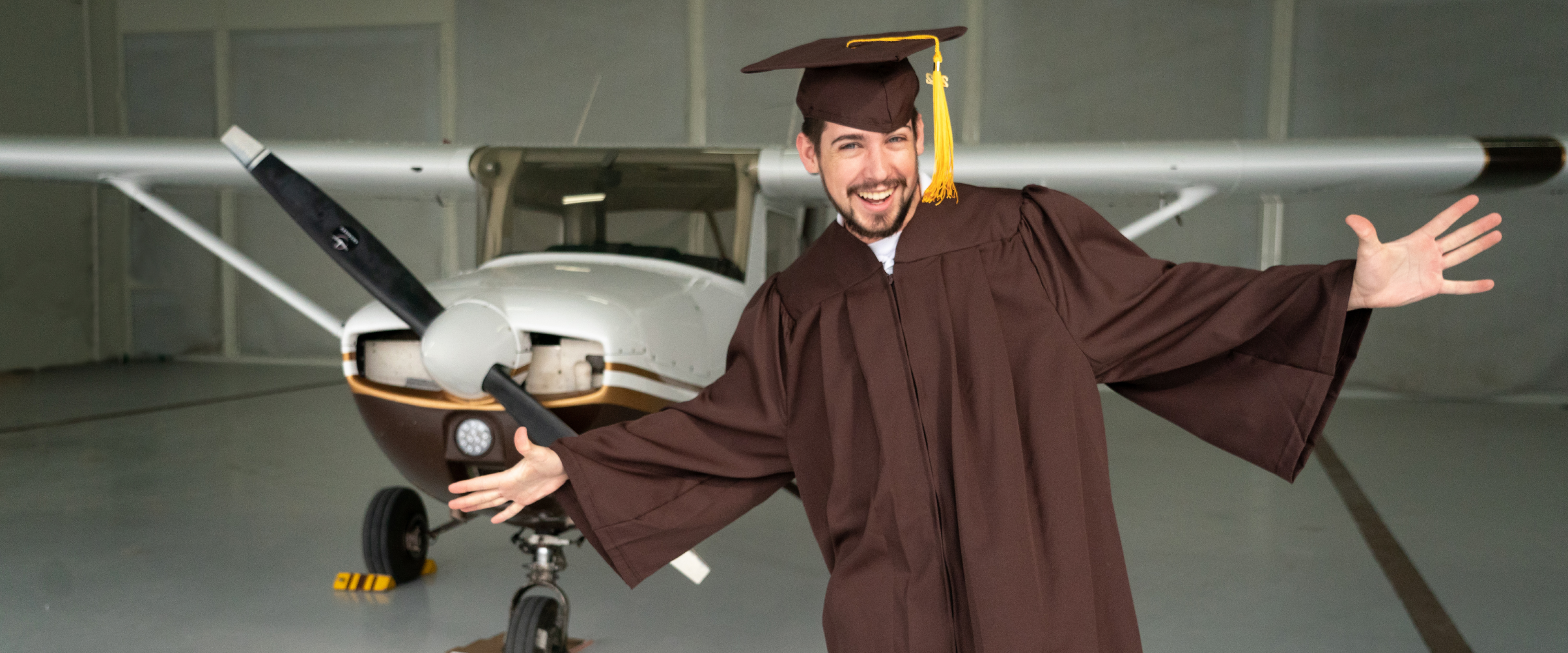 A portrait of Kyle Albrecht in his graduation attire standing in front of a plane.