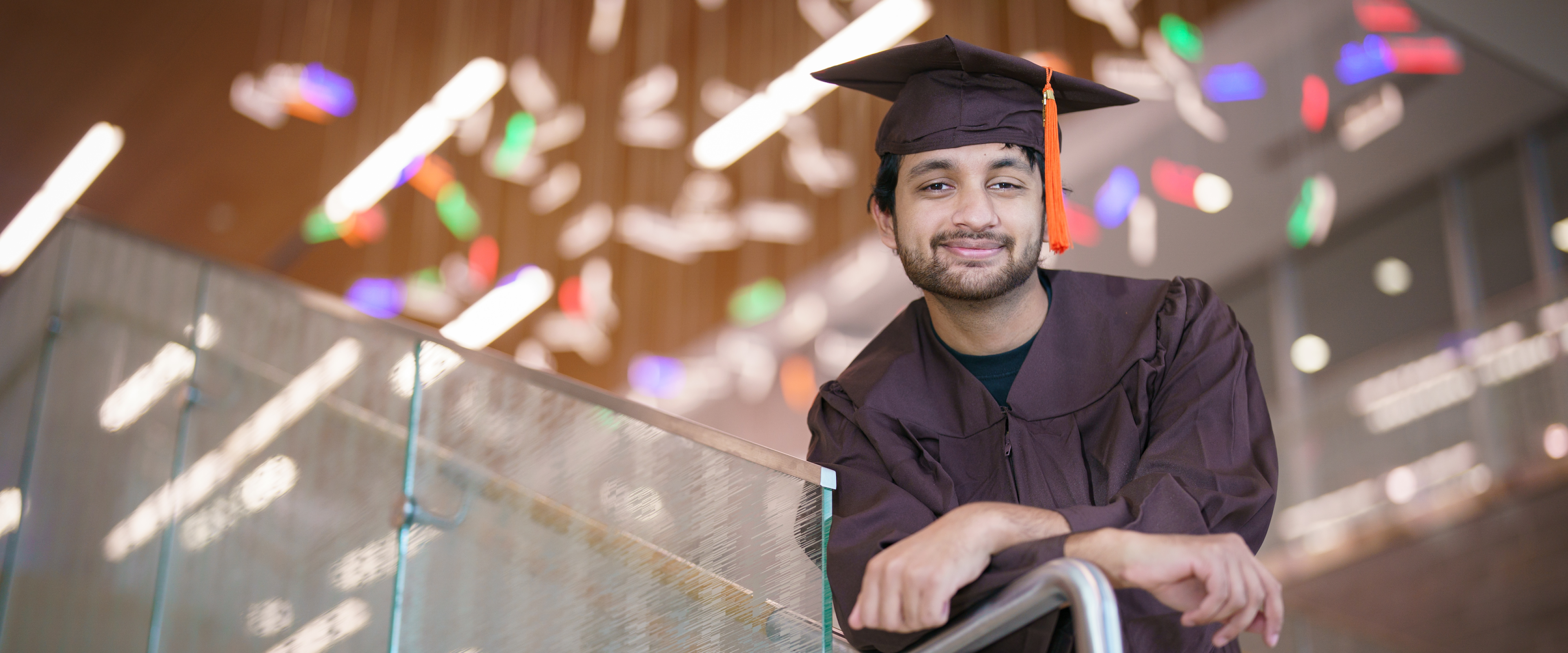 Bharat Goel leans on a railing while wearing his graduation cap and gown.