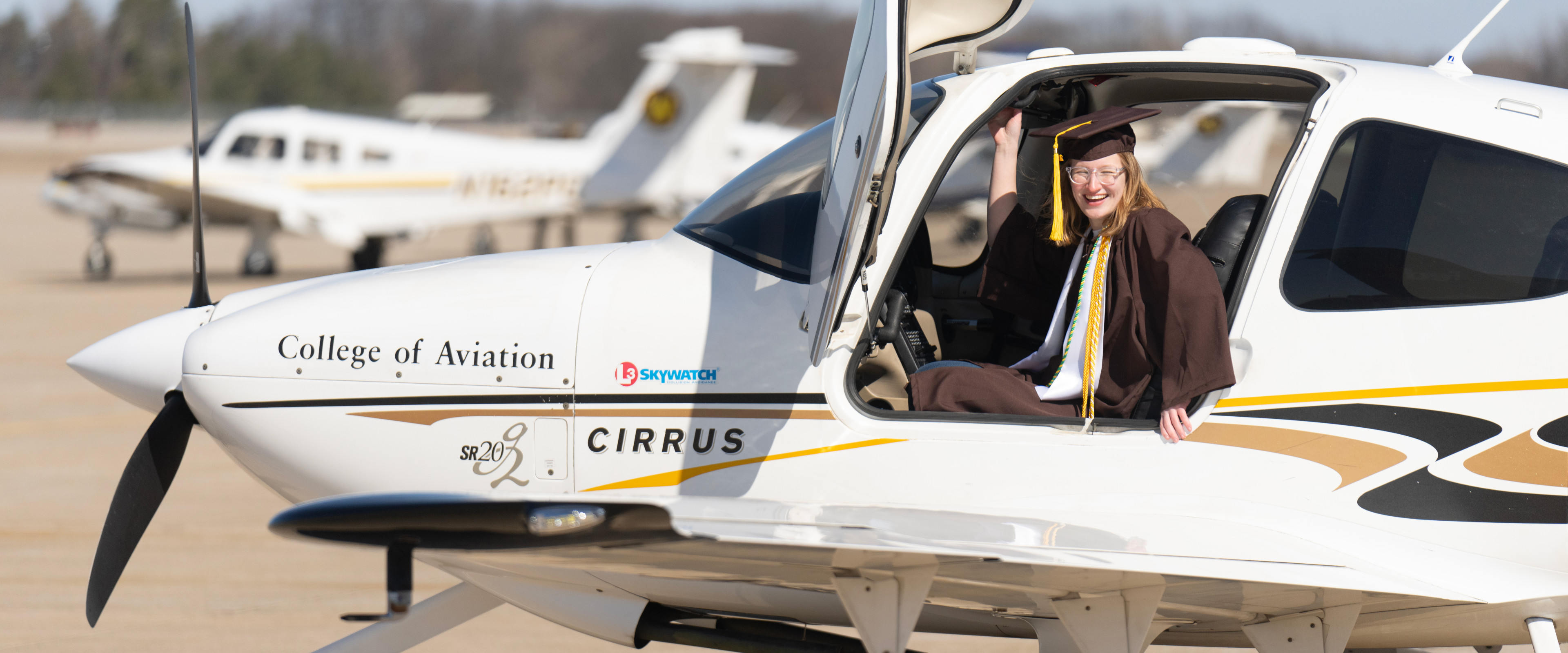 Laila Stein, dressed her graduation cap and gown, sits in the cockpit of a small College of Aviation airplane.