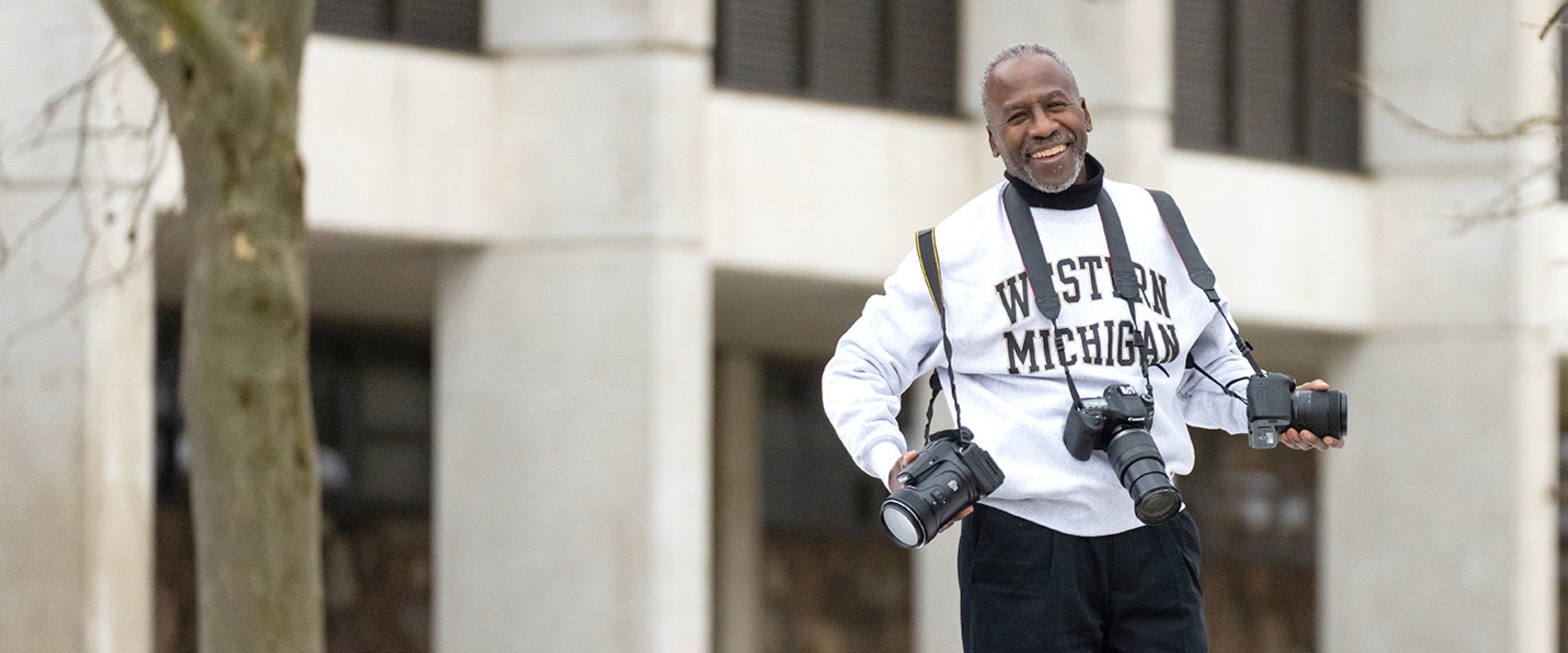 Barry Roberts poses for a picture while holding three different cameras.