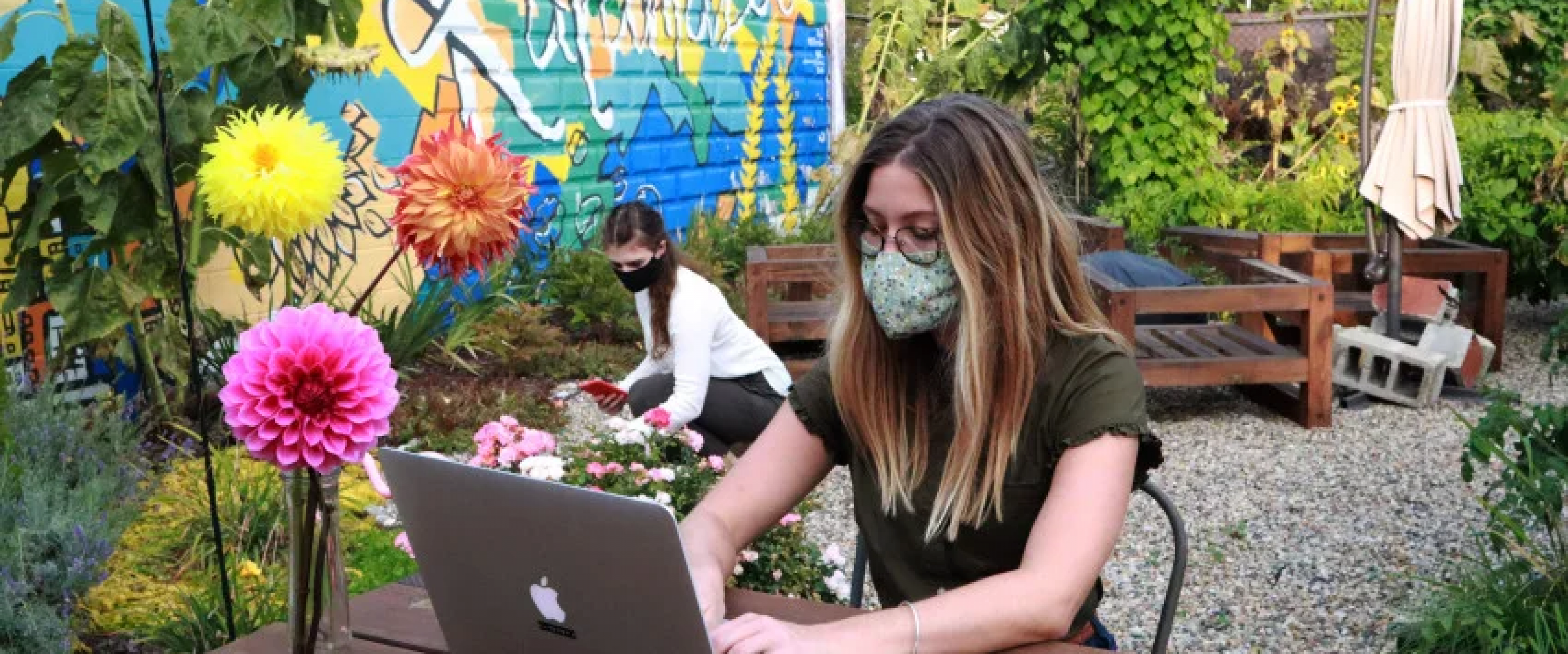 Image of a masked student on a laptop outdoors