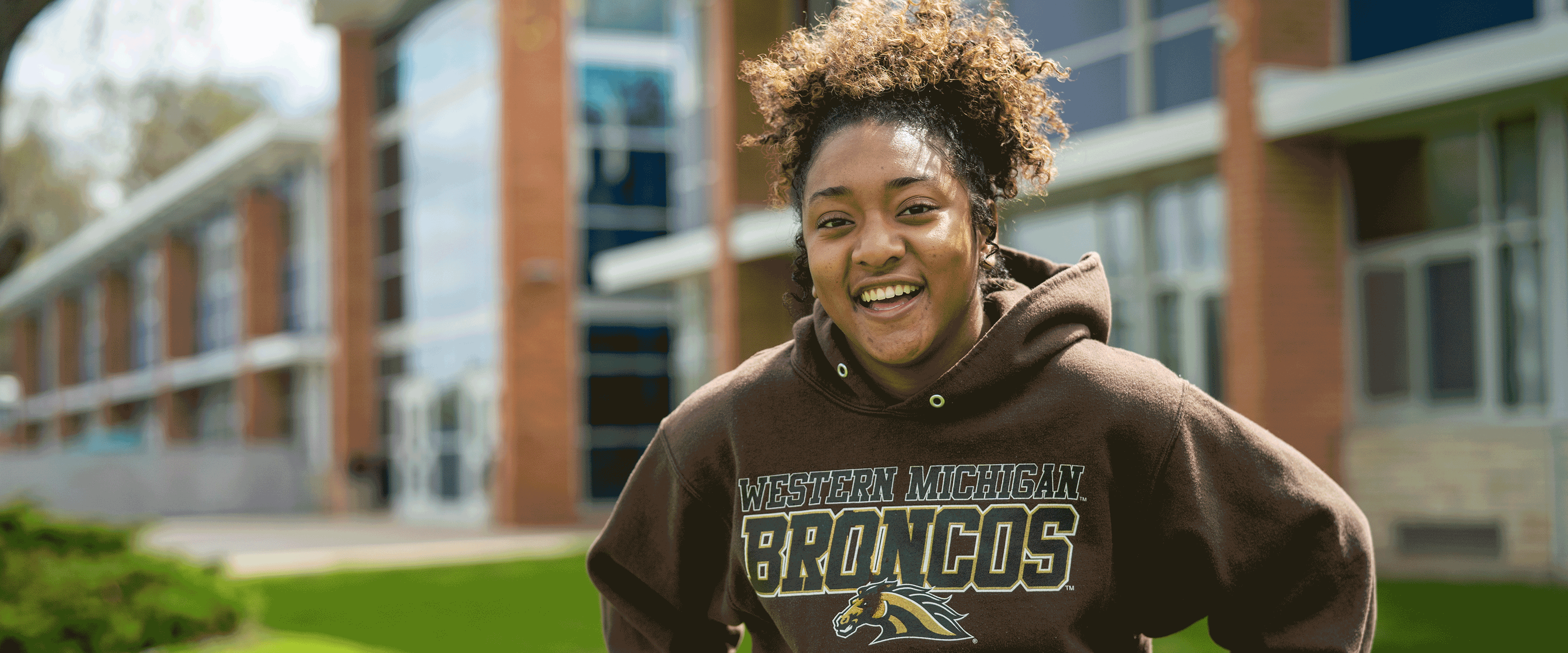 A Merze Tate College student in WMU sweatshirt smiling outdoors