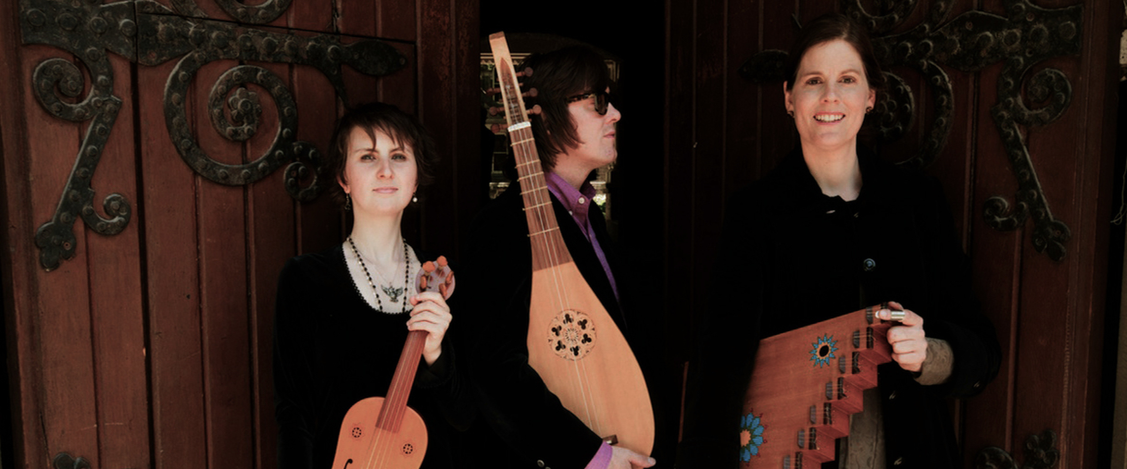 Members of the Pneuma Ensemble stand holding their instruments: a vielle, lute, and psaltery.